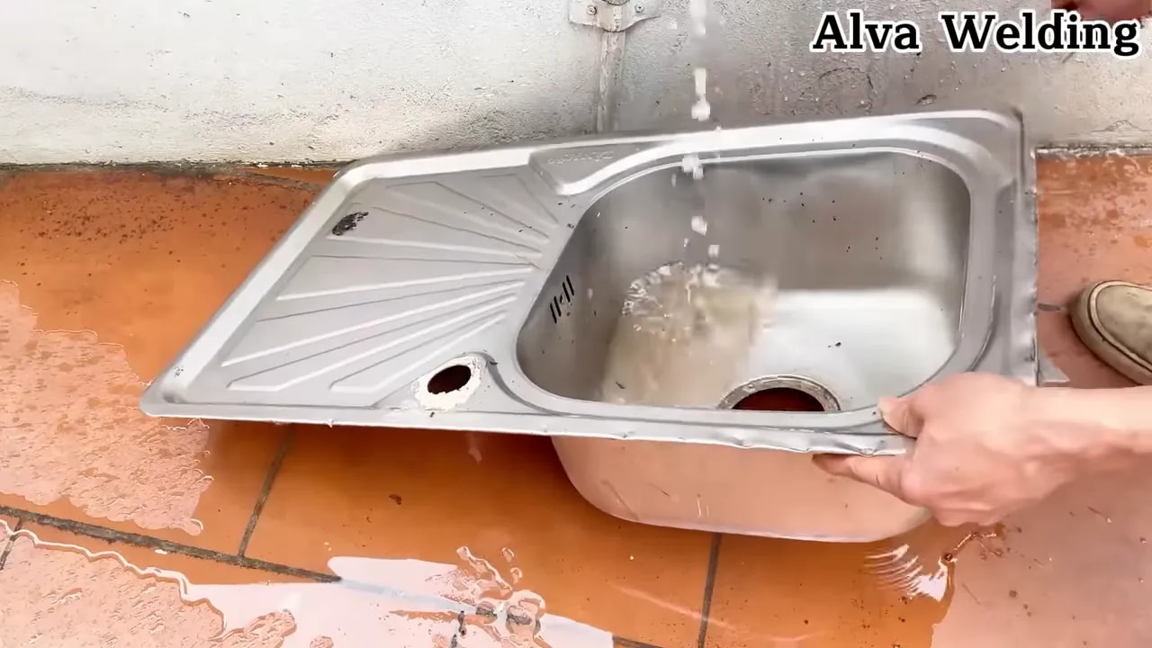 clean stainless sink being rinsed and inspected on a tiled floor