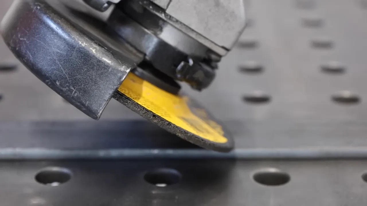 clear close-up of an angle grinder's grinding wheel edge contacting a steel bar at an angle