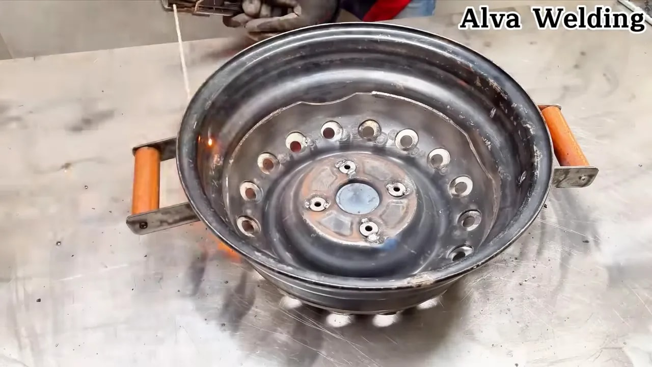 stainless washing machine drum repurposed as a fire pit with side handles glowing with fire